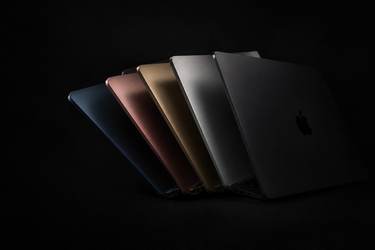 Three laptop lids in dark, gray, and silver anodized aluminum finishes fanned across a soft gradient backdrop