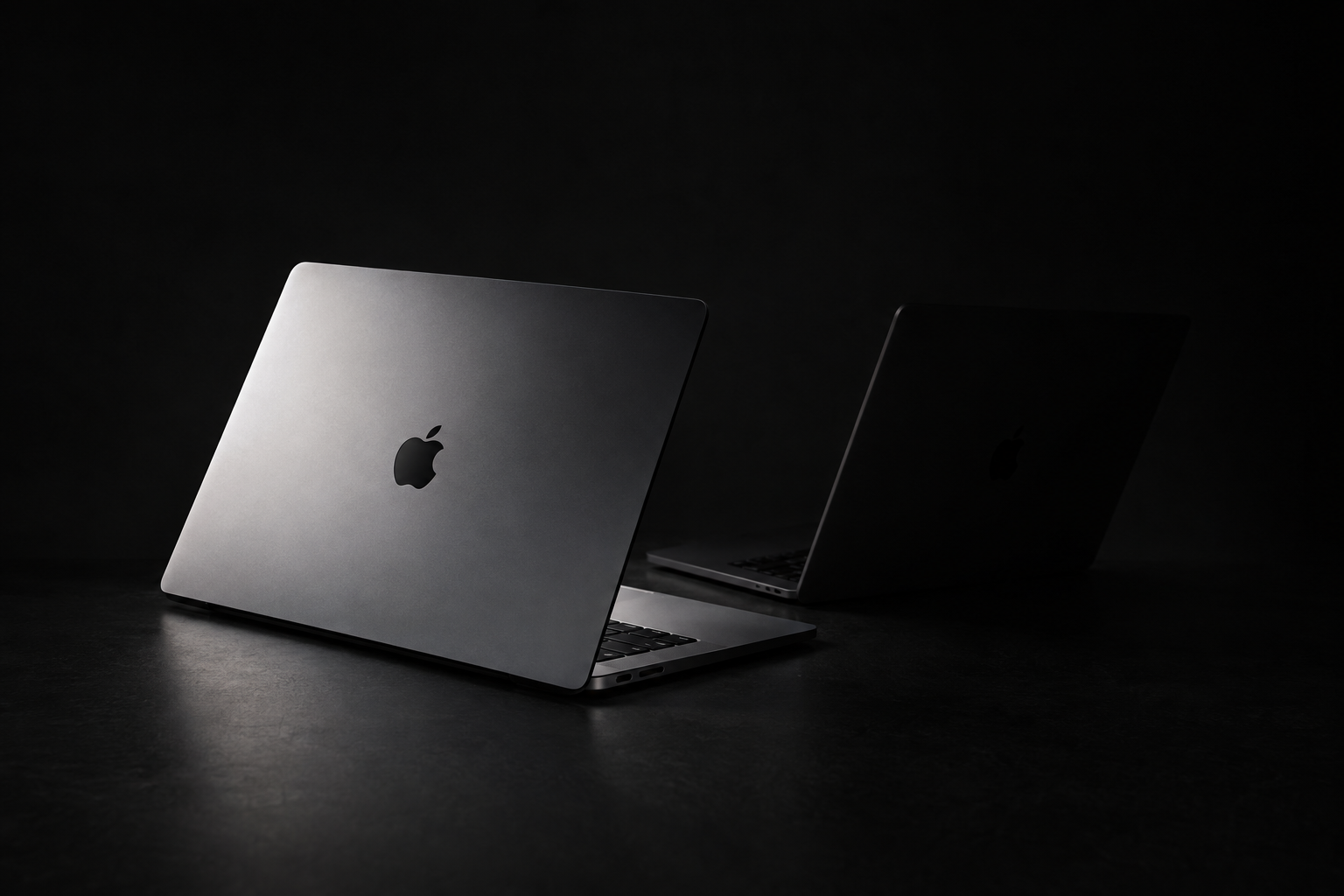 Two similar pro laptops on a gray backdrop, one lit clearly and one in shadow, suggesting a timing decision
