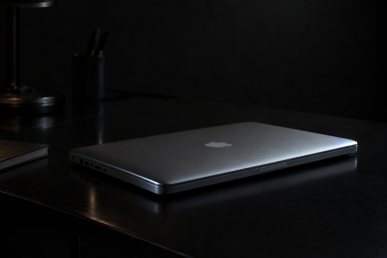 An aluminum MacBook Pro half-closed on a dark gray background, lit by a single soft edge light
