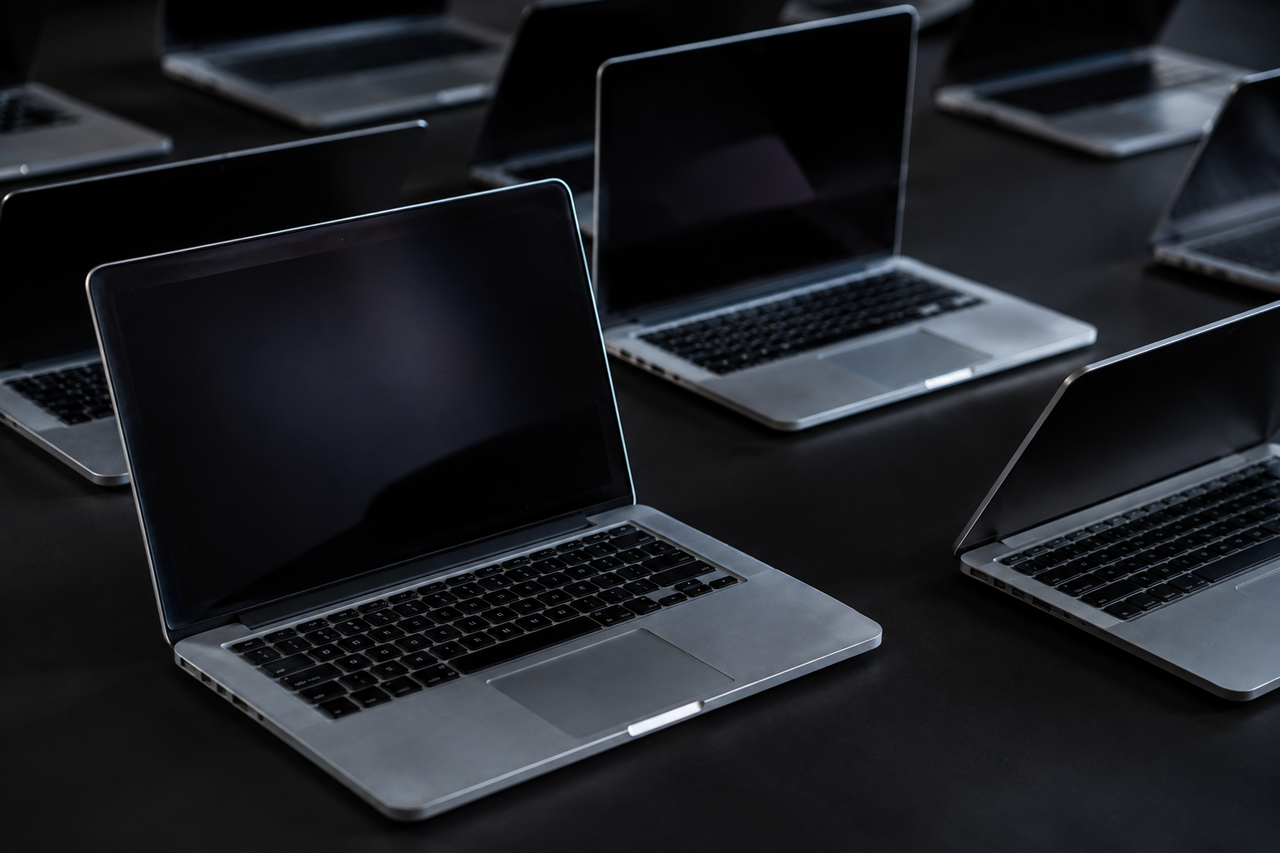 Several used MacBooks arranged in a dark grid, each softly lit, one in sharp focus